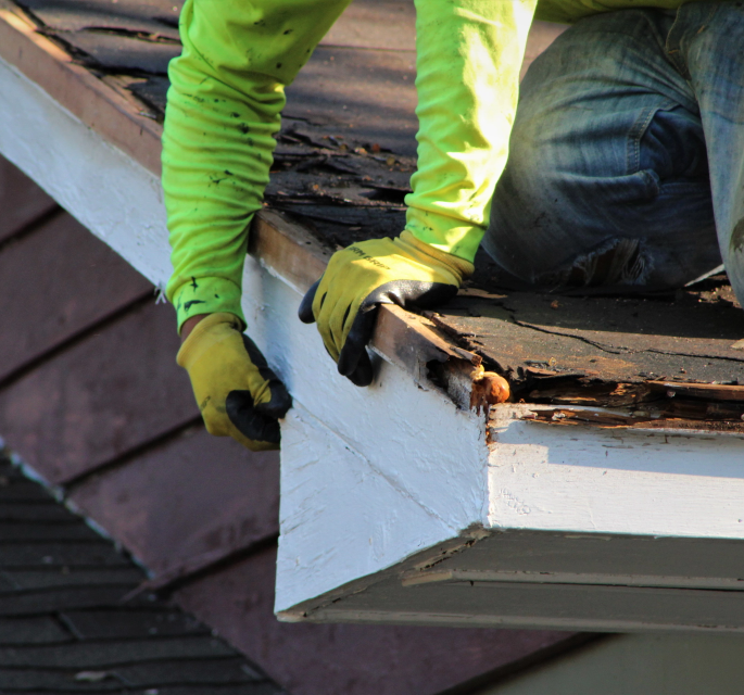 Roofer in protective gear conducting maintenance on a house roof, showcasing essential upkeep to prevent common roofing issues