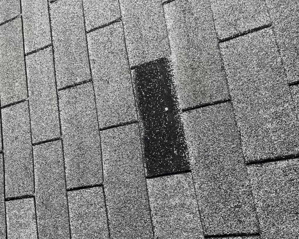 Close-up of shingle roofing with a patch repair indicating common storm damage, emphasizing the need for professional roof repair services.